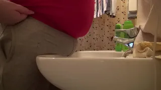 pees through gray pants over the sink in the bathroom