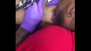 Horny tattoo artist multi-tasking sucking client's nipples