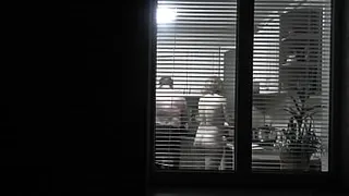 Peeping. Voyeur. Neighbor pervert voyeur in evening on street looks out window as naked sexy neighbor in kitchen prepares dinner for her husband. Naked in public. Naked at home. Family.  Outdoor